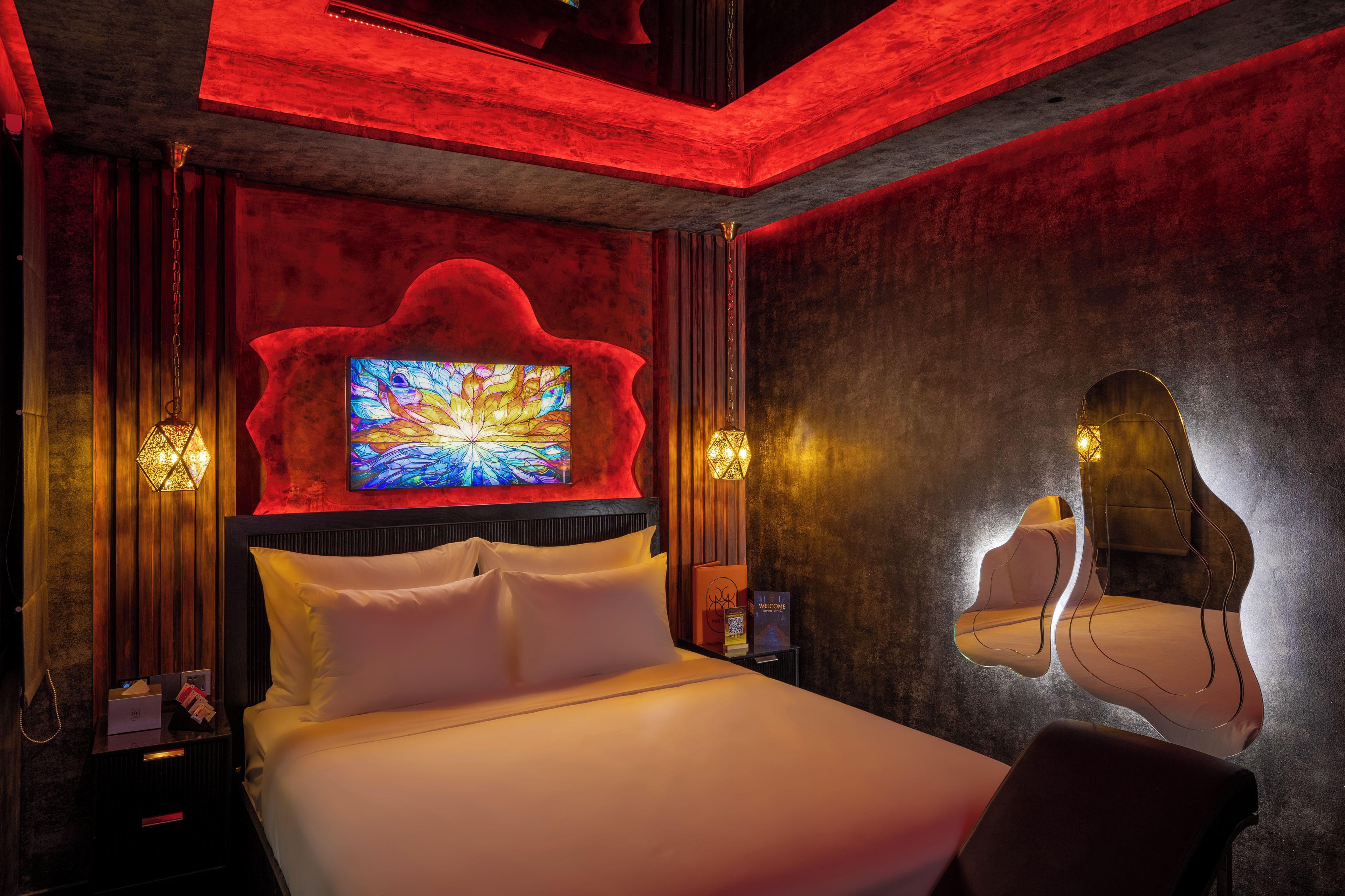 Ein modernes Hotelzimmer mit einem großen Bett, einem an der Wand montierten Fernseher und einem außergewöhnlichen Spiegeldesign.