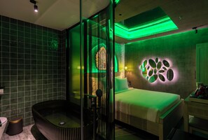 Un baño moderno con ducha envuelta en vidrio, una bañera y una cama con una pared iluminada en verde.