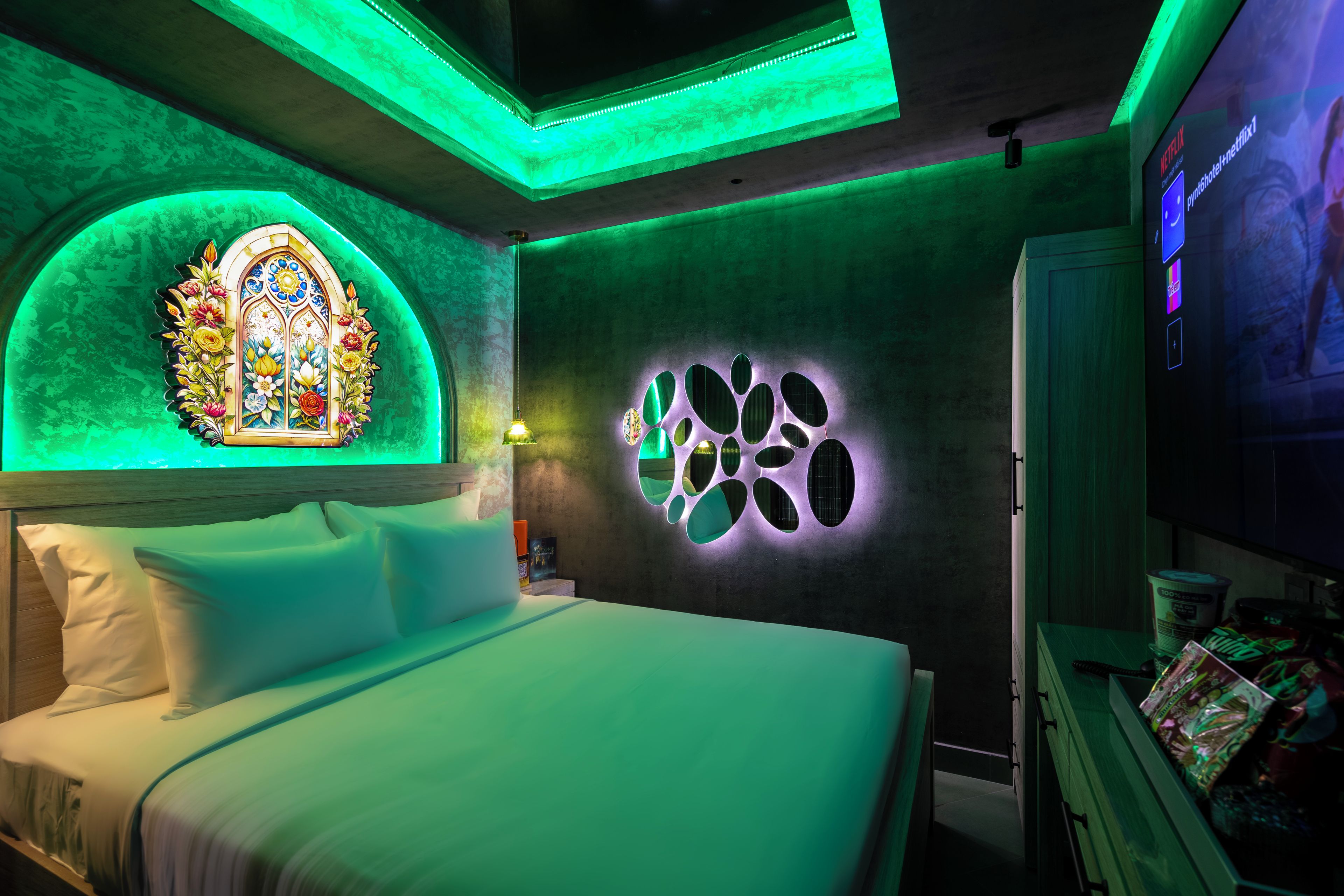 A room with a bed, a stained glass window, a wall with a circular design, and a television screen displaying a Netflix interface.