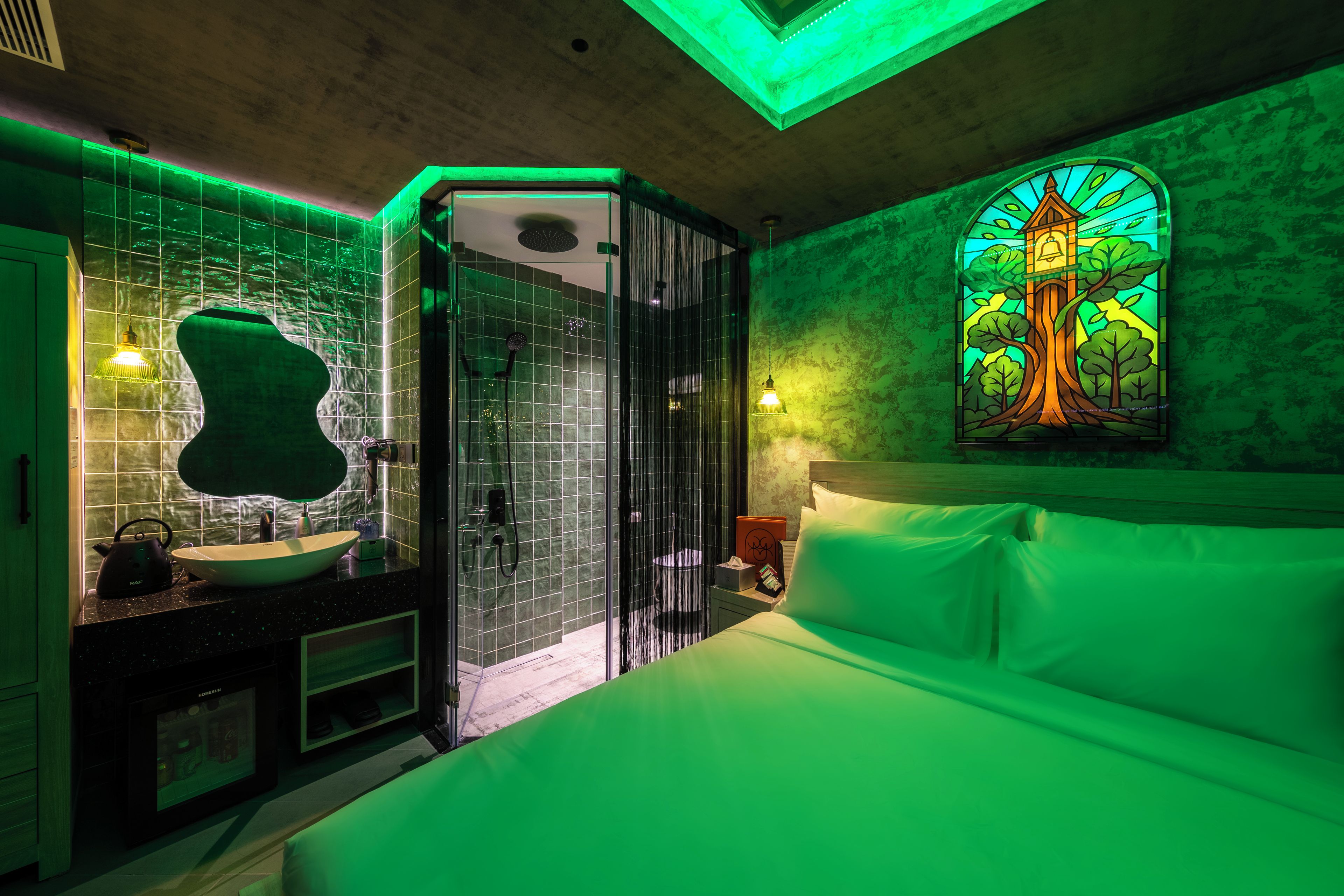 A modern bathroom with a glass-enclosed shower, a sink with a mirror, and a bed with a green-lit window.
