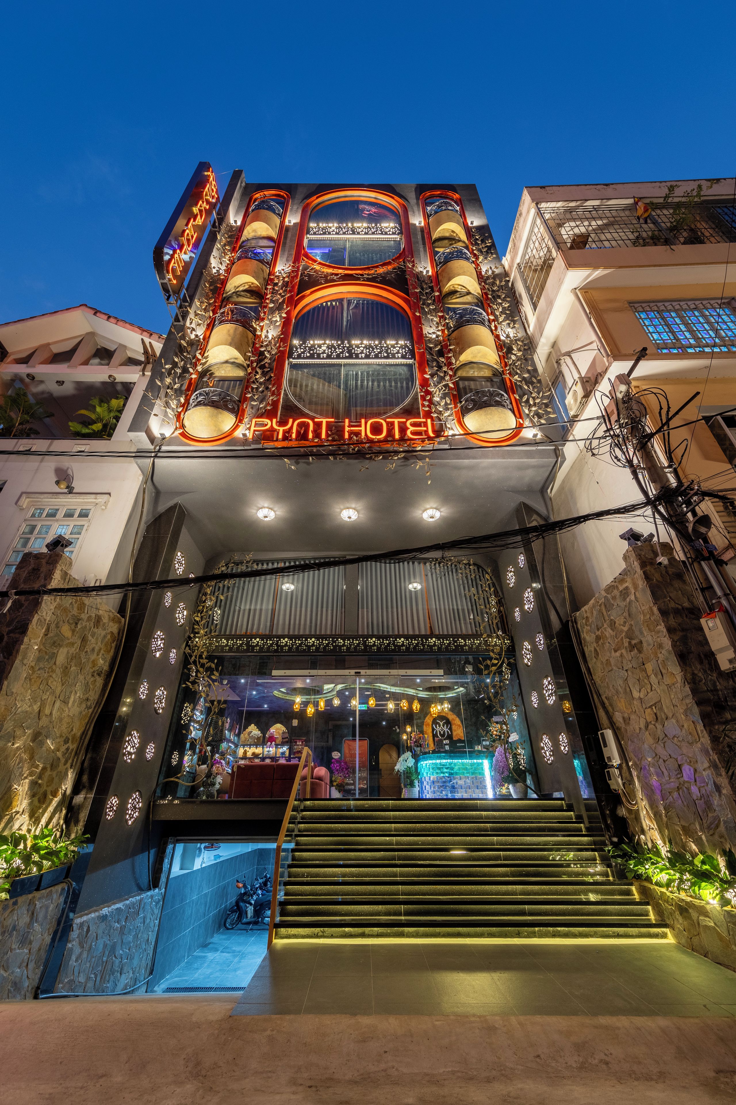 A hotel entrance with a neon sign, a staircase, and a shop at the bottom.