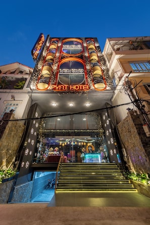 A hotel entrance with a neon sign, a staircase, and a shop at the bottom.