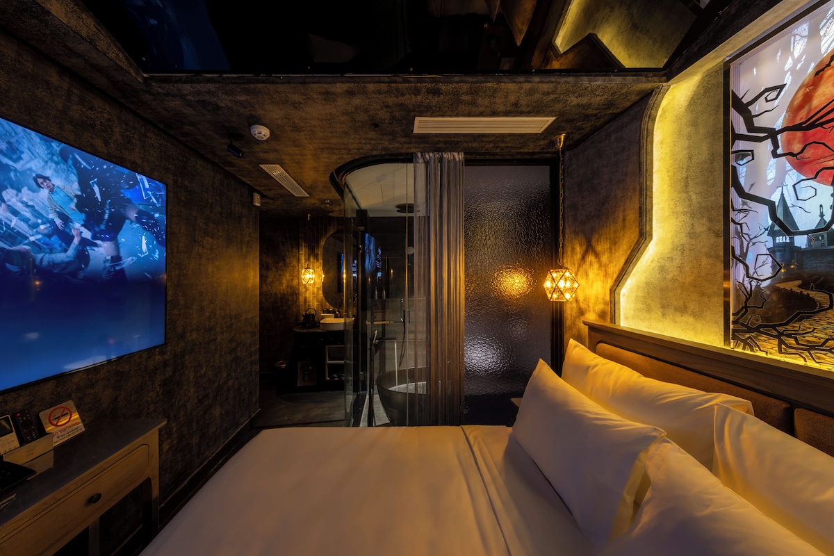 A hotel room with a large bed, a TV, a bathroom with a glass door, and a painting on the wall.