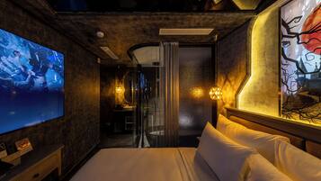 A hotel room with a large bed, a TV, a bathroom with a glass door, and a painting on the wall.