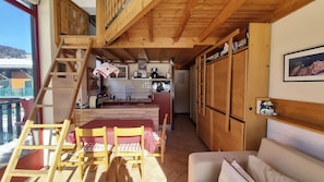A cozy interior with a dining area, kitchen, and a balcony with a wooden railing. - Jatoba - apartment - 4 people - ski-in/ski-out (Les Gets)