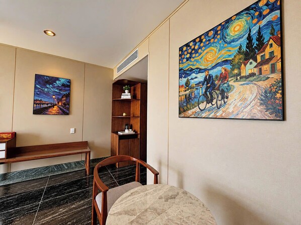 A hotel lobby with a marble floor, a wooden bench, a seating area with a chair, a bookshelf, and two paintings on the wall.