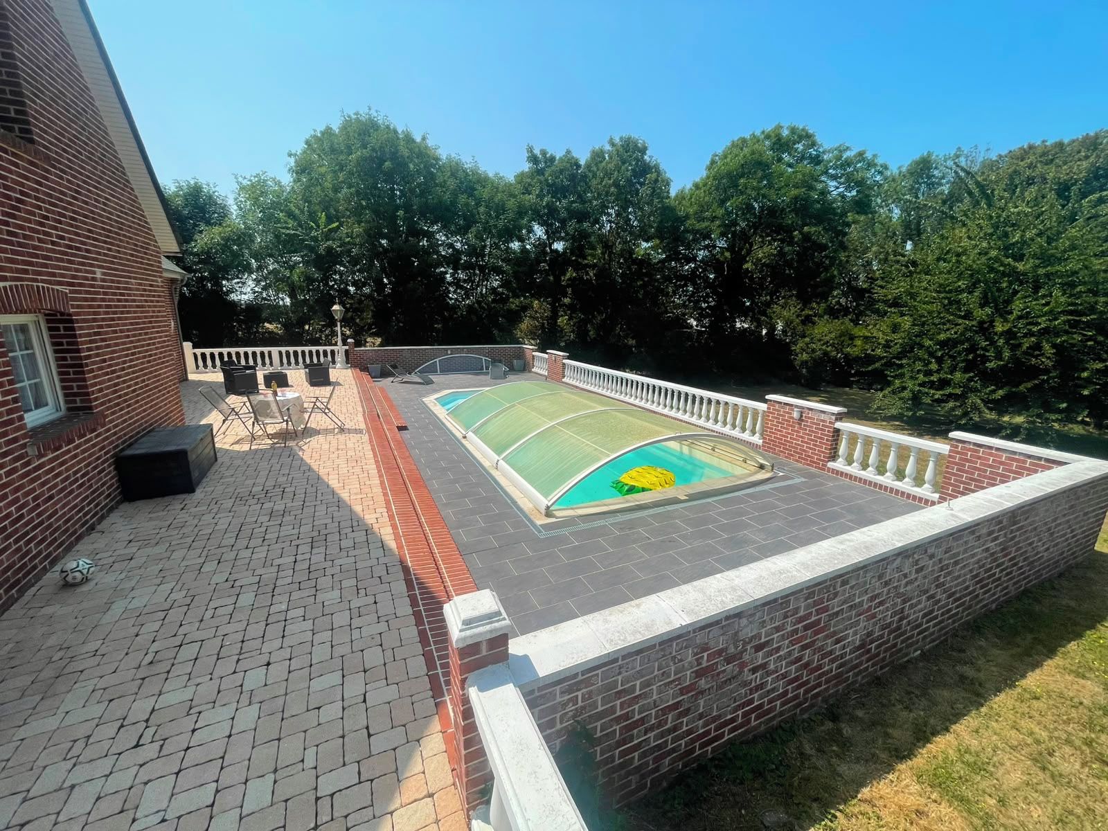 An outdoor swimming pool with a sunshade, surrounded by a brick wall and a white railing.