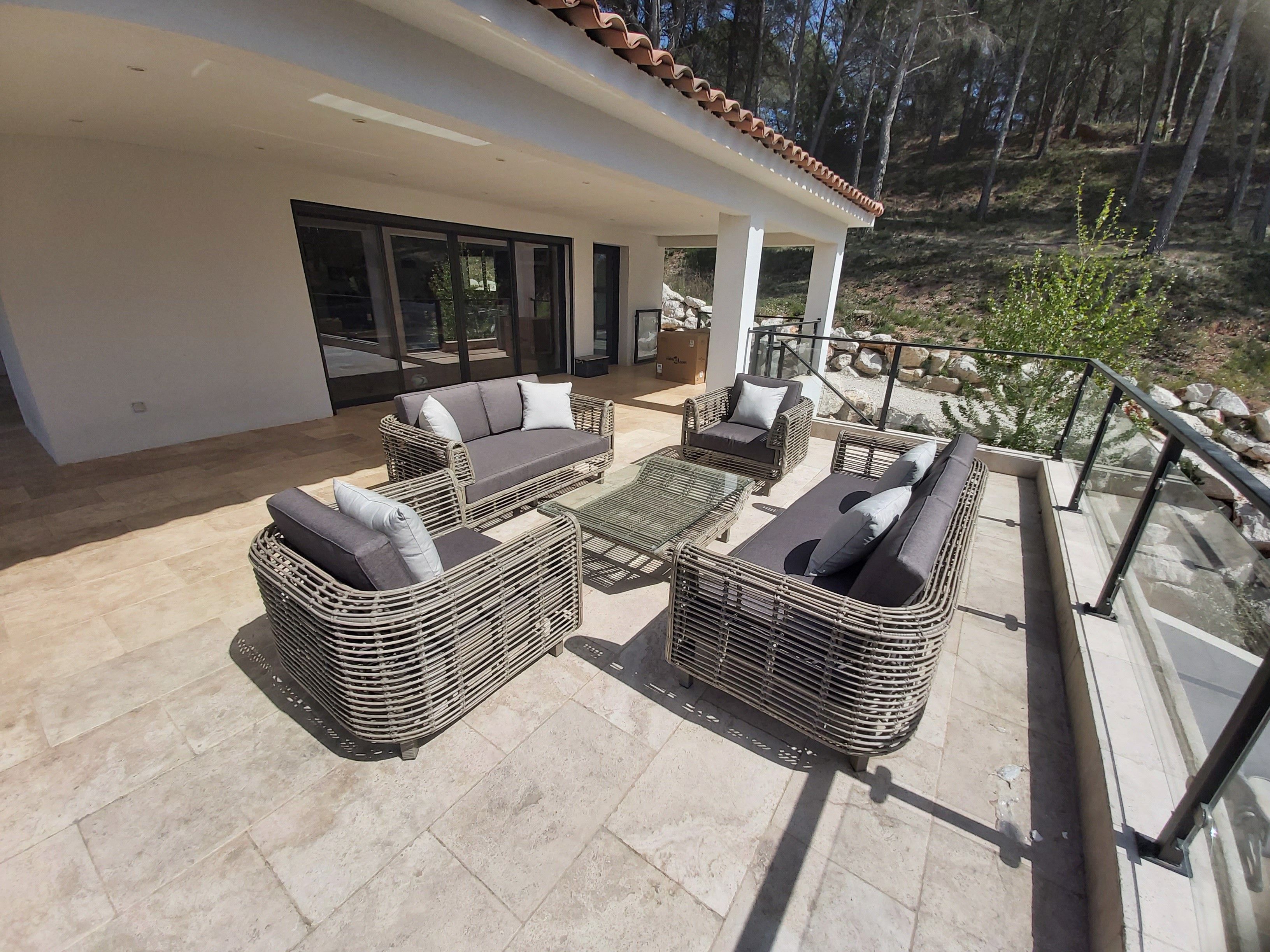 Un espacio de estar al aire libre cubierto con muebles de mimbre y una mesa de vidrio, con vistas a un paisaje rocoso.