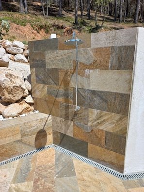A shower area with stone tiles and a metal showerhead.
