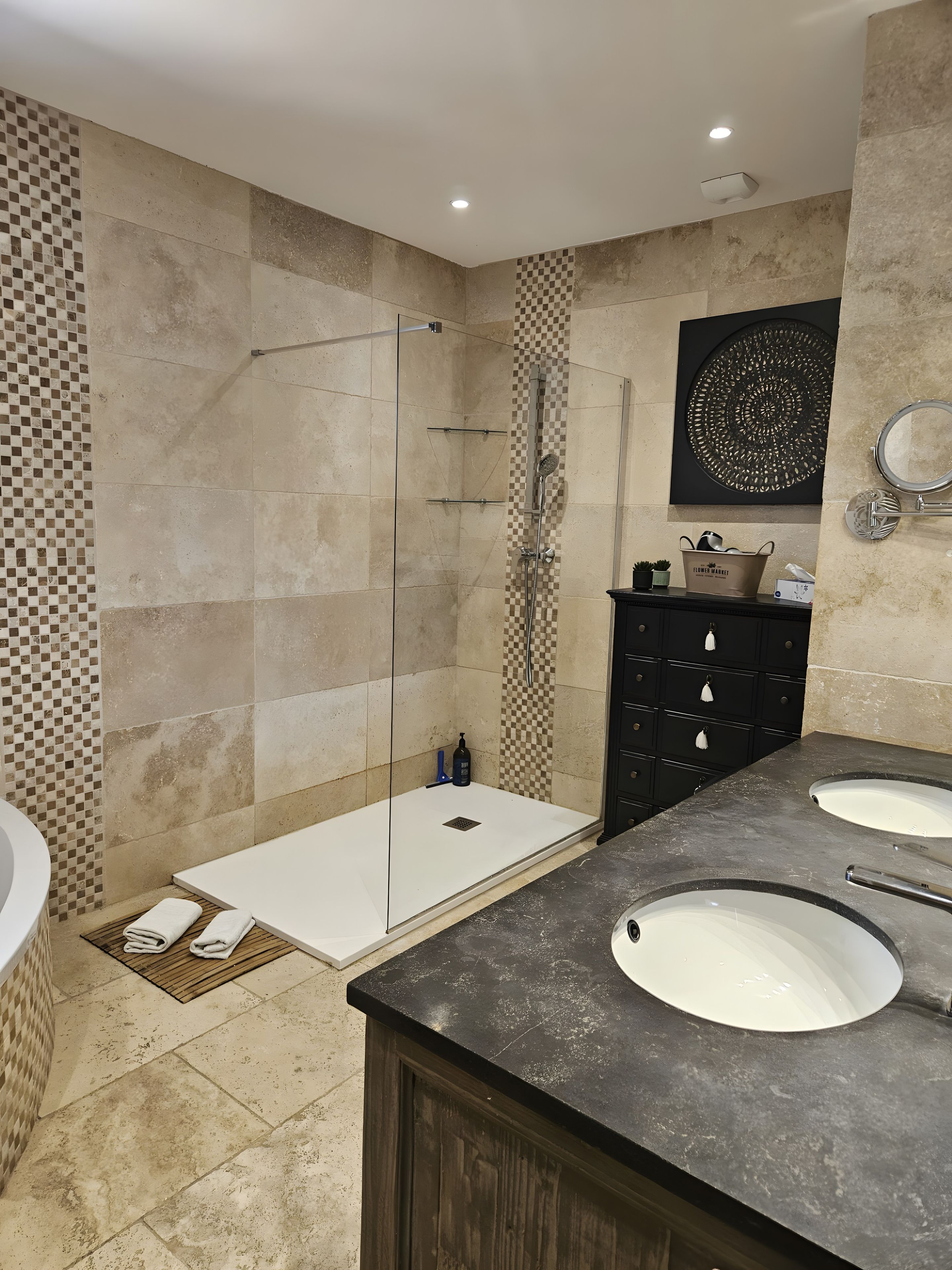 Een moderne badkamer met een douche in een glazen cabine, twee wastafels en een donker houten wastafelmeubel.