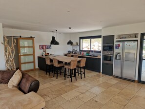 Een moderne keuken met een centraal eiland, barkrukken, een eettafel en een koelkast.