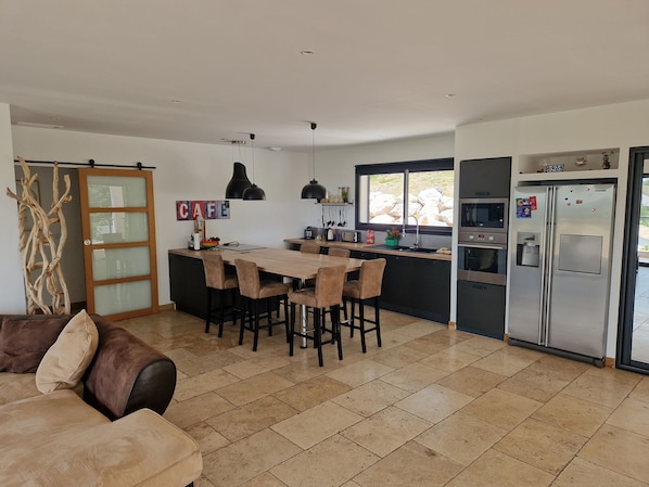 A modern kitchen with a central island, bar stools, a dining table, and a refrigerator.