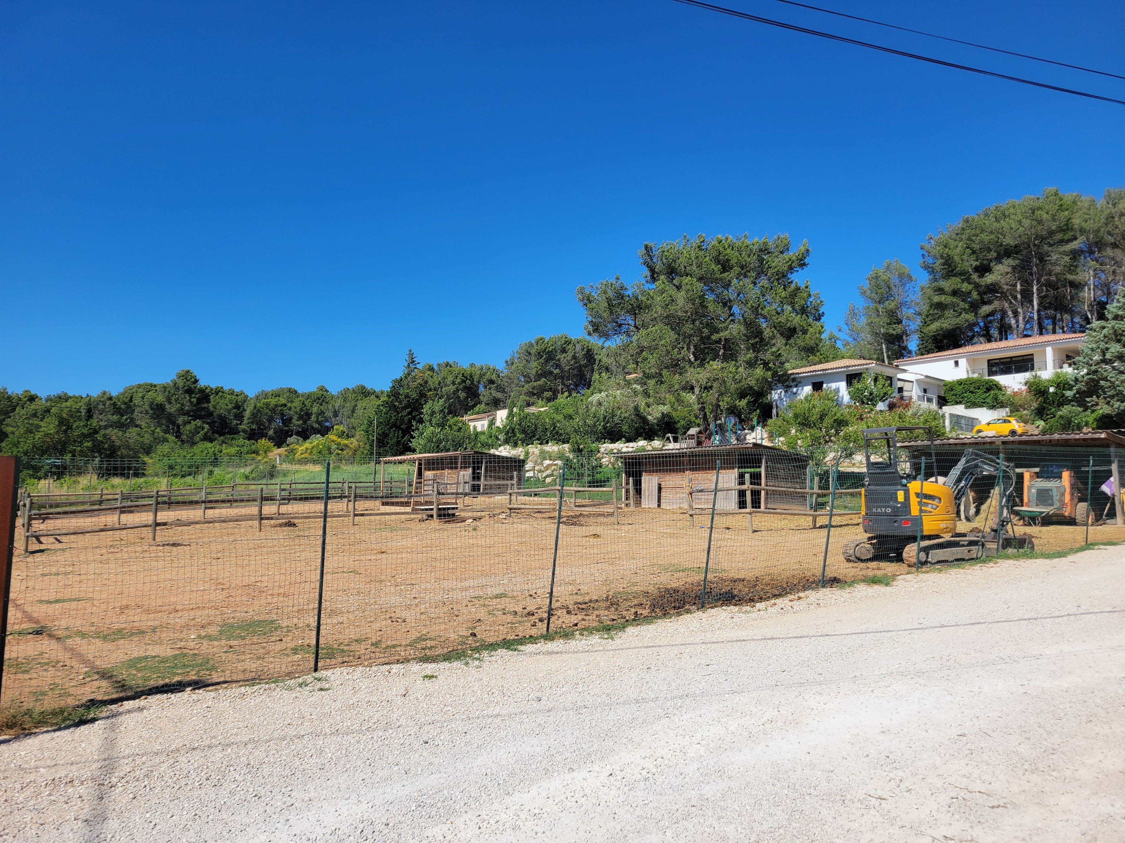 Un espace extérieur clos, avec un chemin de gravier, une petite construction et un véhicule jaune.