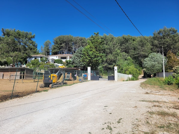 A gravel road leading to a gated area with construction equipment and a fenced enclosure.