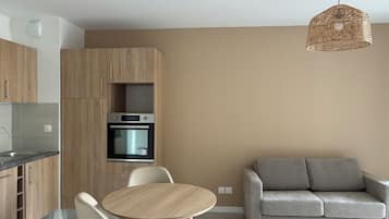 A modern kitchen with wooden cabinets, a built-in oven, and a round dining table with chairs.