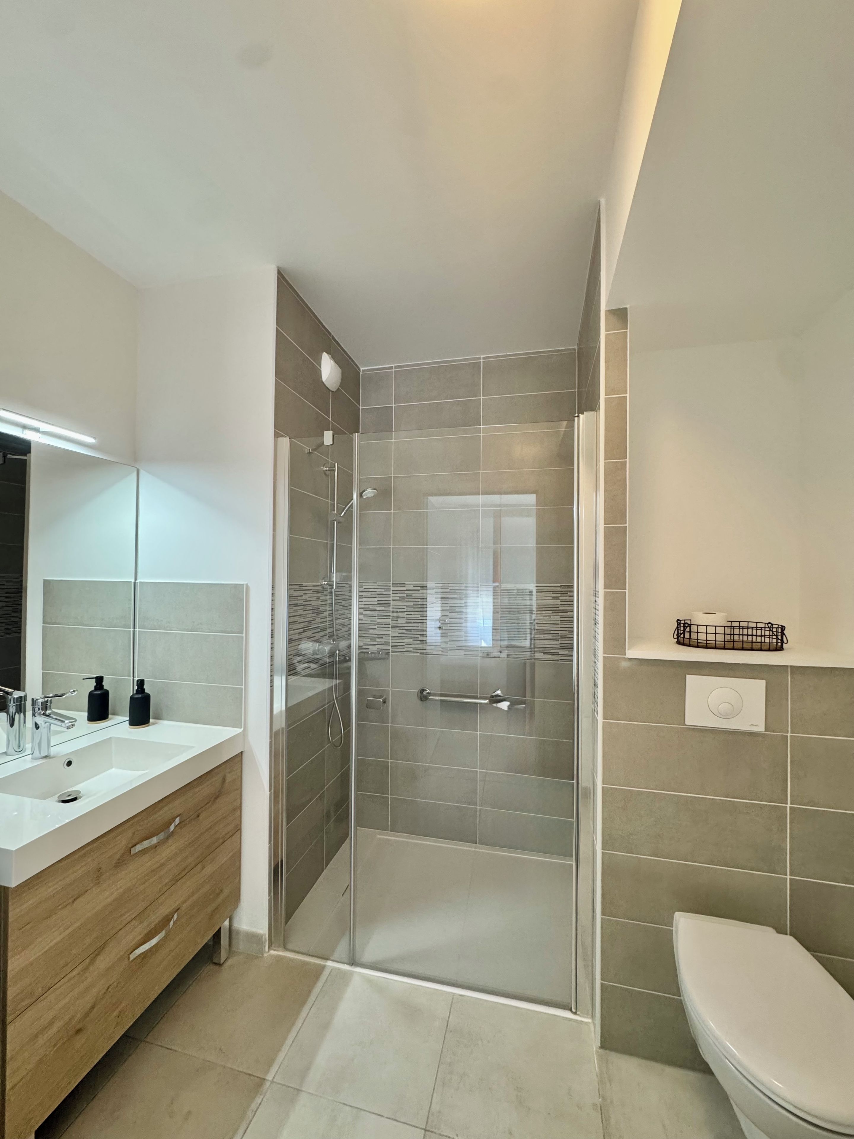 Ein modernes Badezimmer mit einer gläsernen Duschkabine, einem weißen Waschbecken und einer Toilette.