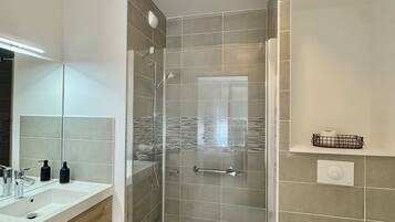 Ein modernes Badezimmer mit einer gläsernen Duschkabine, einem weißen Waschbecken und einer Toilette.