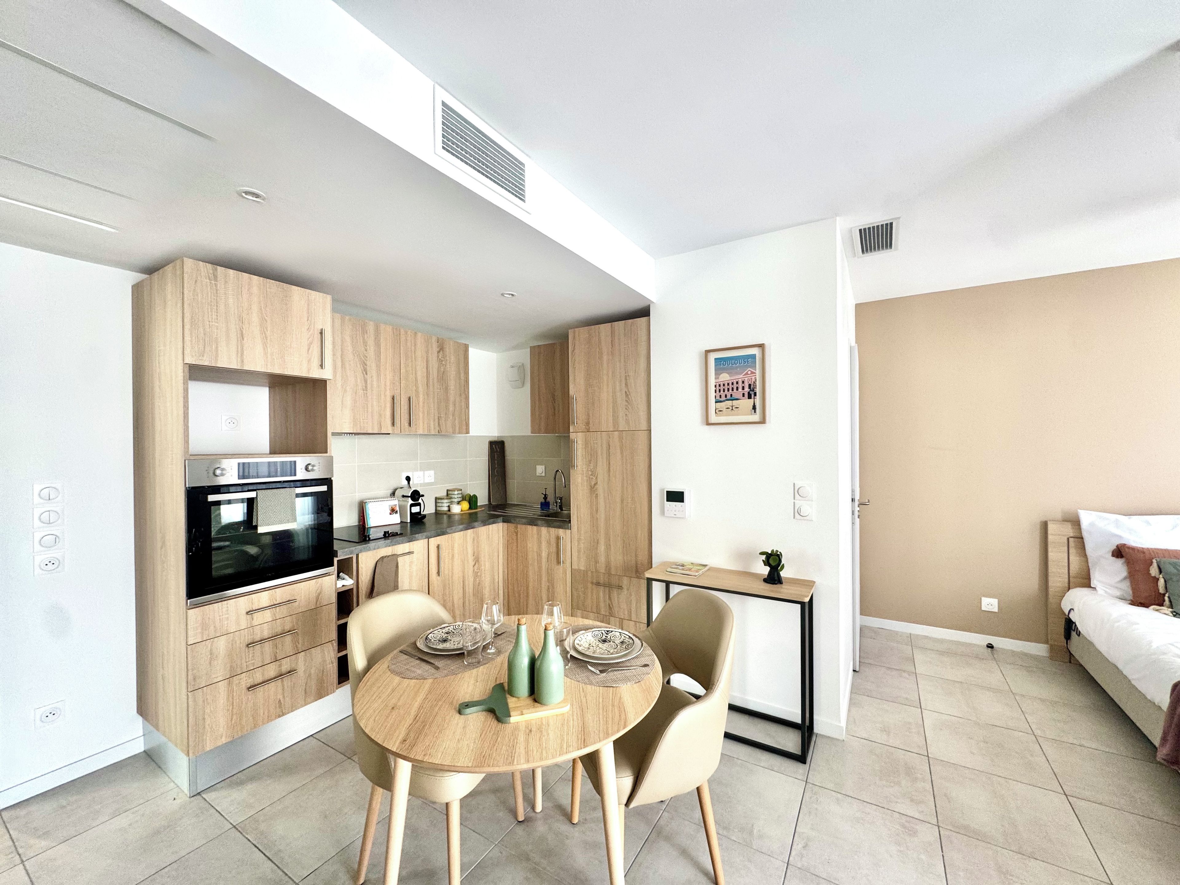 A modern kitchen with built-in appliances, a dining area with a round table, and a bed in the adjacent room.
