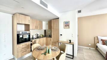 A modern kitchen with built-in appliances, a dining area with a round table, and a bed in the adjacent room.