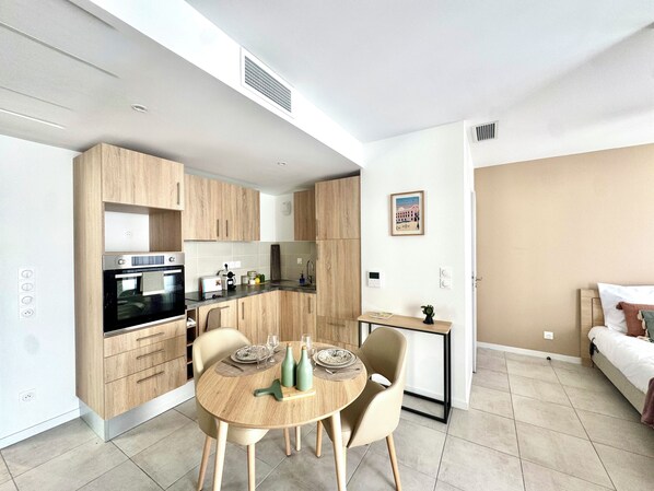 Una cocina moderna con electrodomésticos integrados, un comedor con mesa redonda y una cama en la habitación contigua.