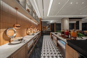 A modern hotel lobby with a long reception desk, a mirror, and a coffee station.