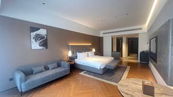 A modern hotel room with a bed, a sofa, a small table, and a wall-mounted TV.