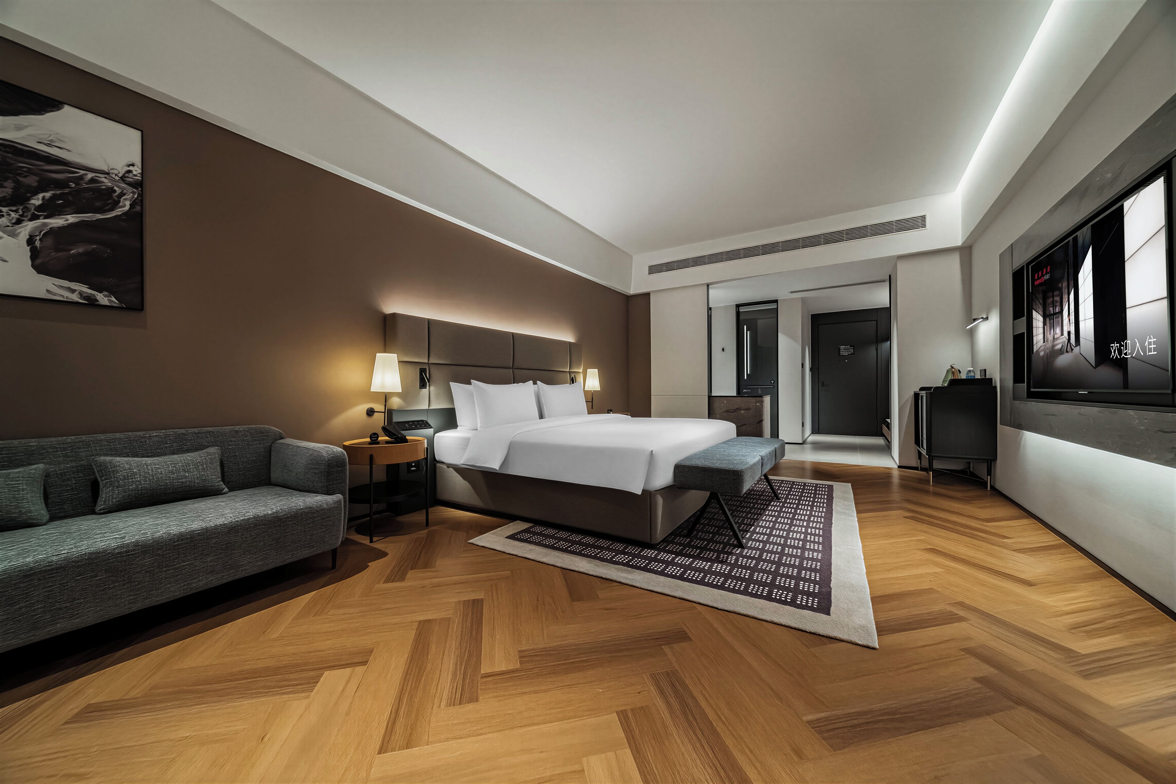 A modern hotel room with a large bed, a sofa, a desk, and a television.