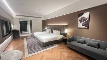 A modern hotel room with a large bed, a sofa, a desk, and a flat-screen TV.
