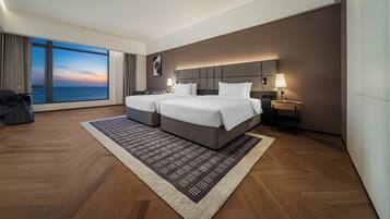 Habitación de hotel moderna con un ventanal grande, dos camas, una mesita de noche y vista al mar.
