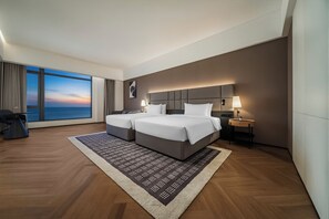 A modern hotel room with a large window, two beds, a nightstand, and a view of the sea. - HUA RUI HOTEL (Sihanoukville)