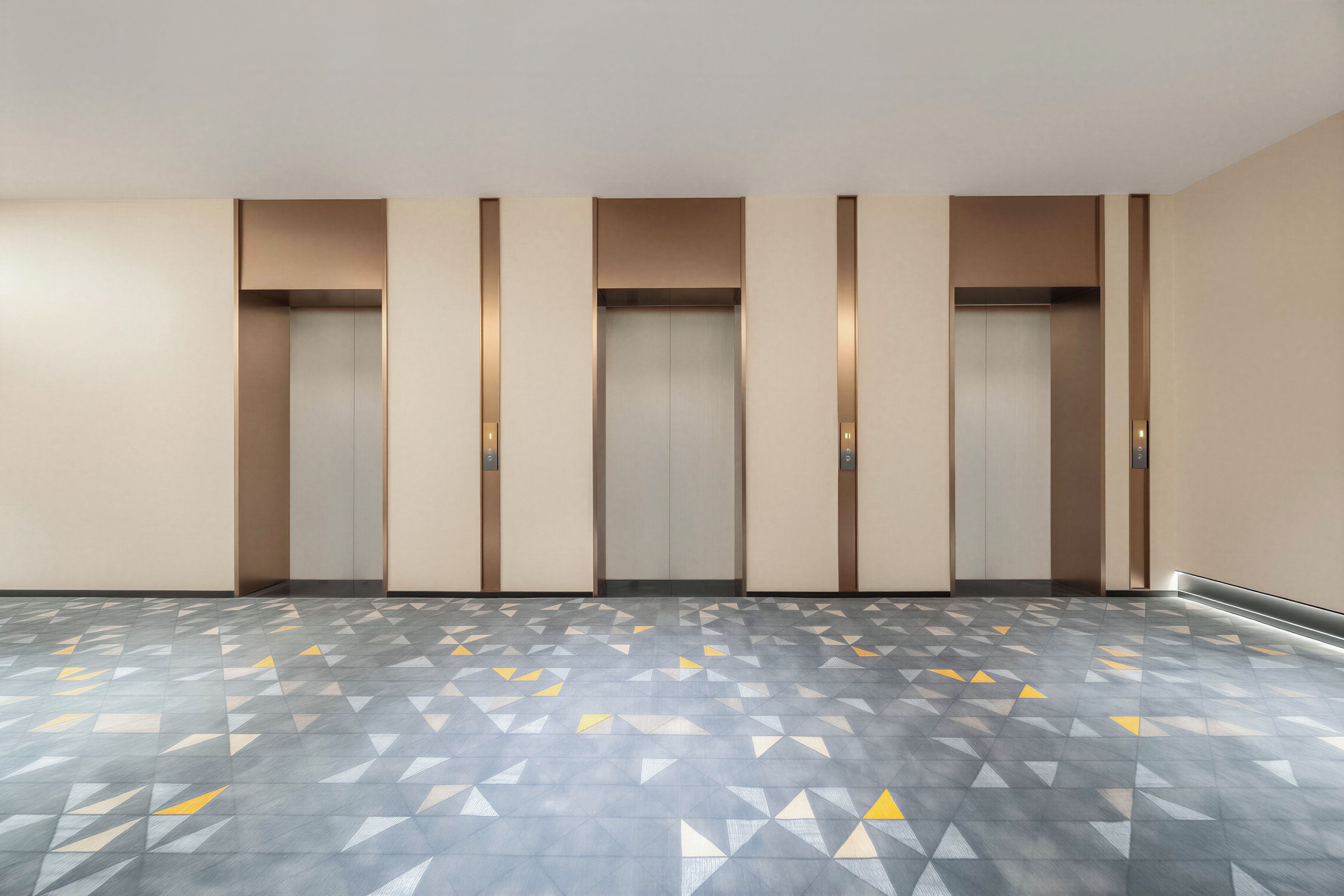 A hallway with five elevators, each with a control panel on the wall. The floor has a geometric pattern.