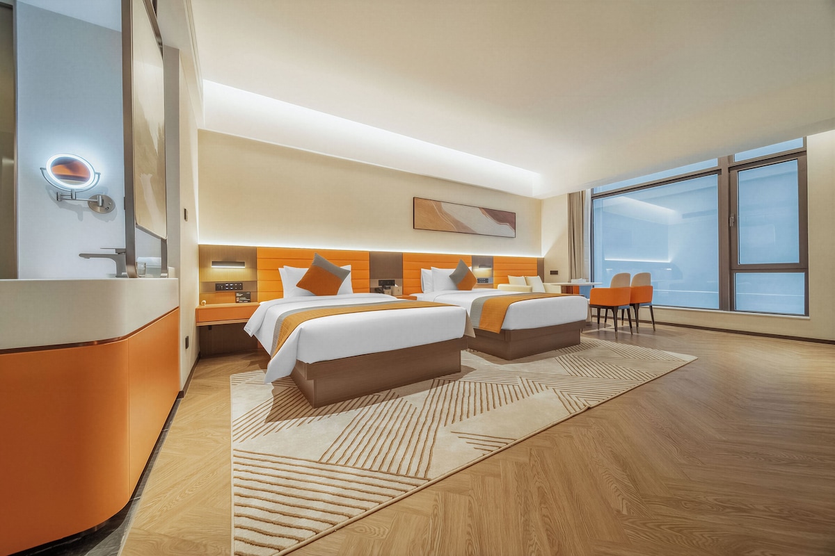 A modern hotel room with a large bed, bedside tables, a mirror, and a view of the city.