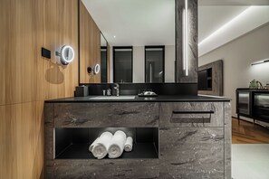 A modern bathroom with a wooden vanity, a built-in towel rack, and a mirror with integrated lighting.