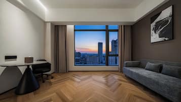 Una habitación de hotel moderna con un gran ventanal, un escritorio, una silla, un sofá y un cuadro en la pared.
