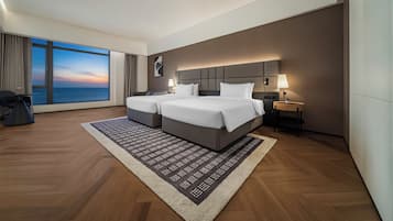 Ein modernes Hotelzimmer mit großem Fenster, zwei Betten, einem Nachttisch und Blick aufs Meer.