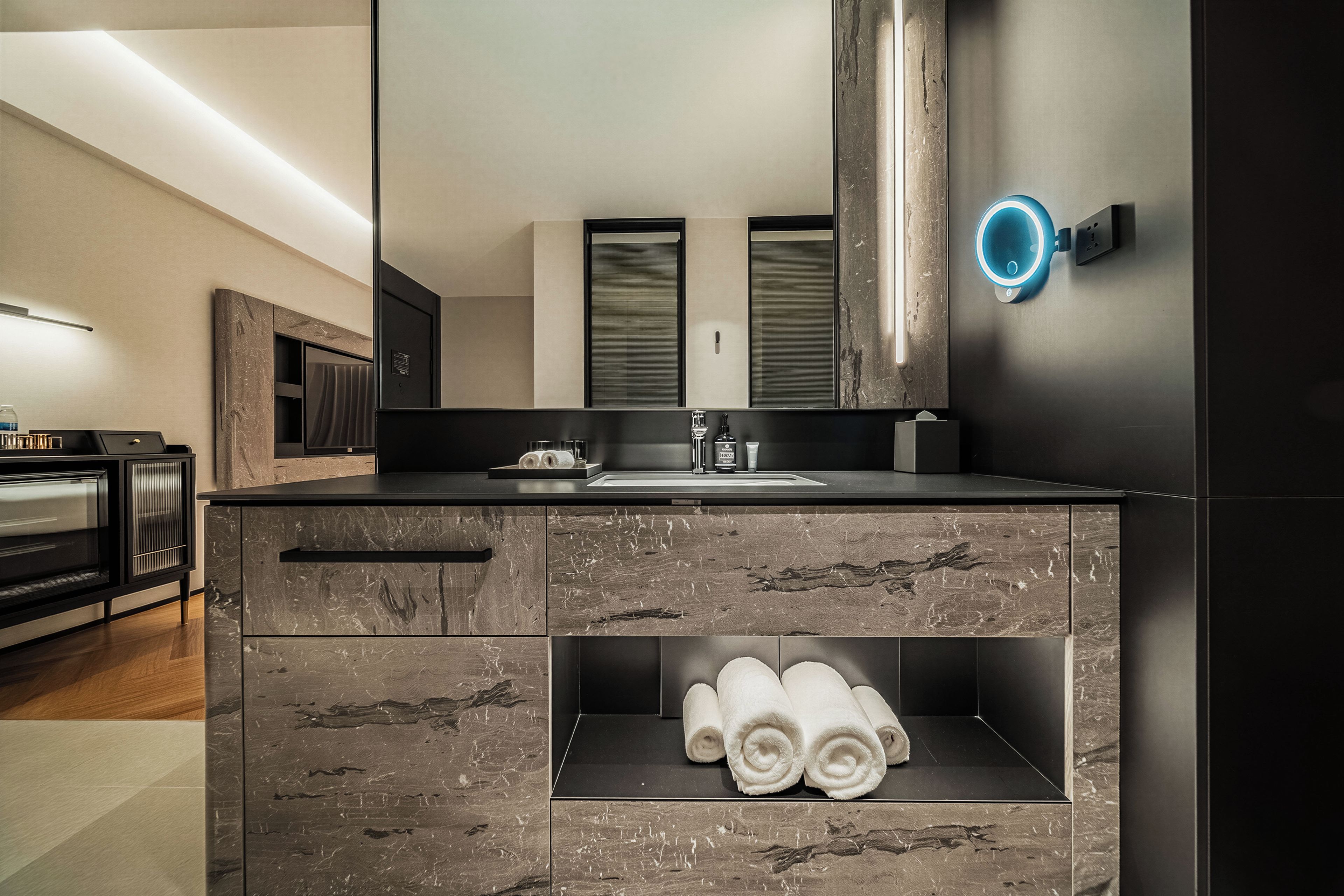 A modern bathroom with a large mirror, a built-in sink, and a towel shelf.