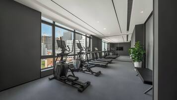 Un gimnasio moderno con diversos equipos de ejercicio, ventanas amplias y vistas a la ciudad.