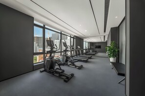 A modern gym with various exercise equipment, large windows, and a view of the cityscape.