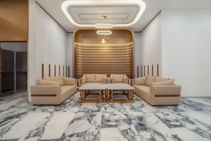 A modern living room with a sofa set, a marble floor, and a unique ceiling design.