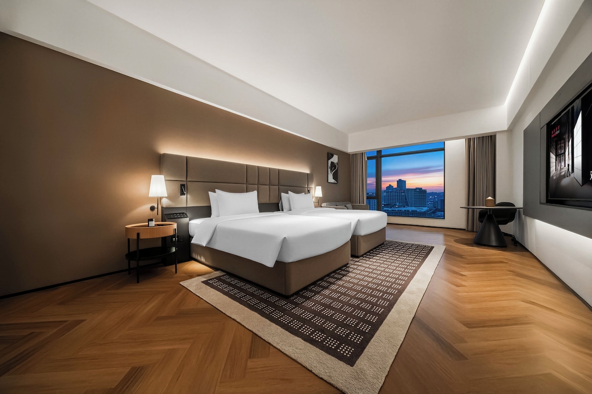 A modern hotel room with a large bed, a city view, and a well-lit ambiance.