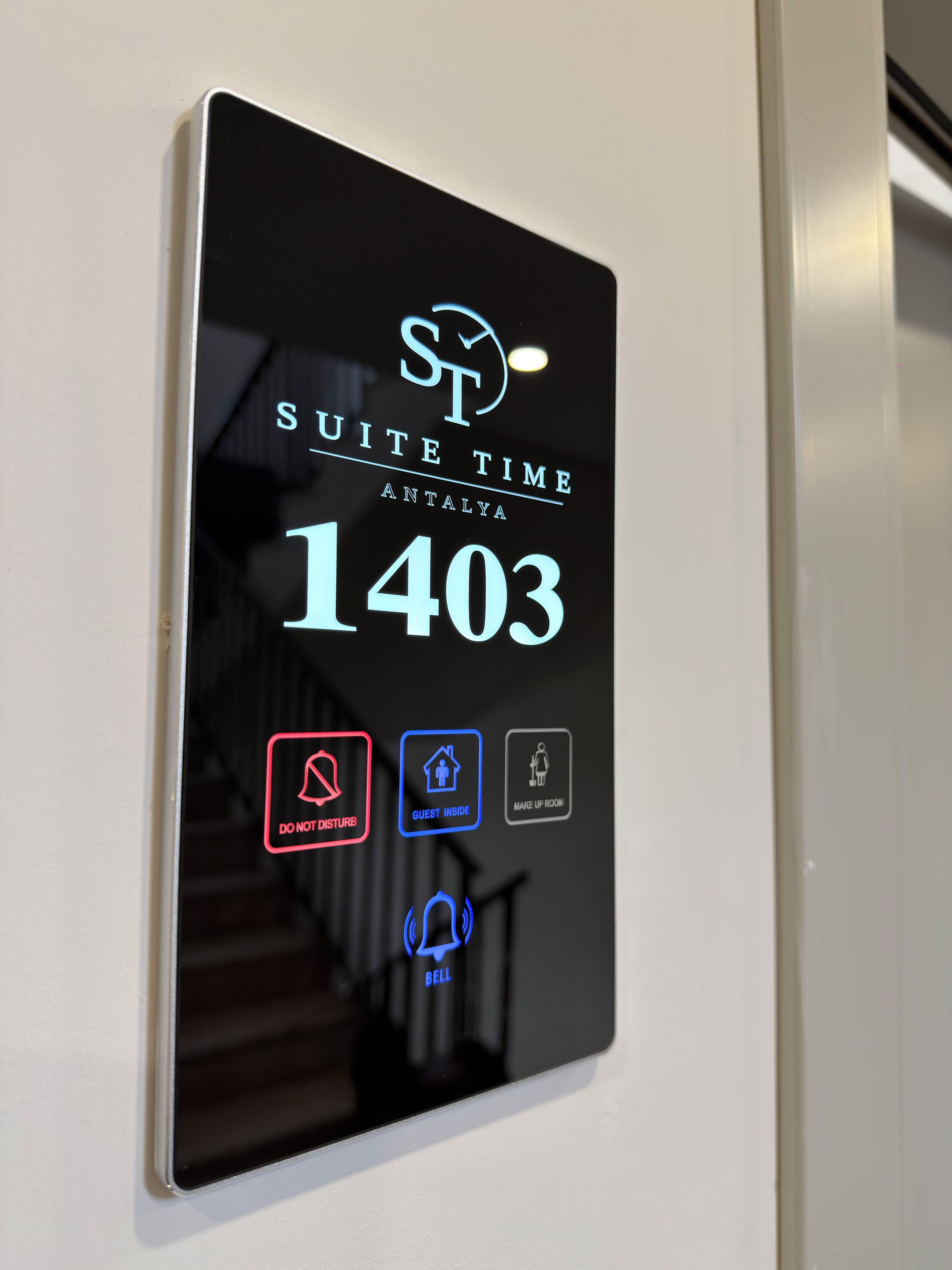 Pantalla digital con el texto 'SUITE TIME ANTALYA 1403' e iconos que indican 'NO MOLESTAR', 'HUESPED EN EL INTERIOR', 'SERVICIO DE HABITACIÓN' y 'SERVICIO DE PORTERÍA'.