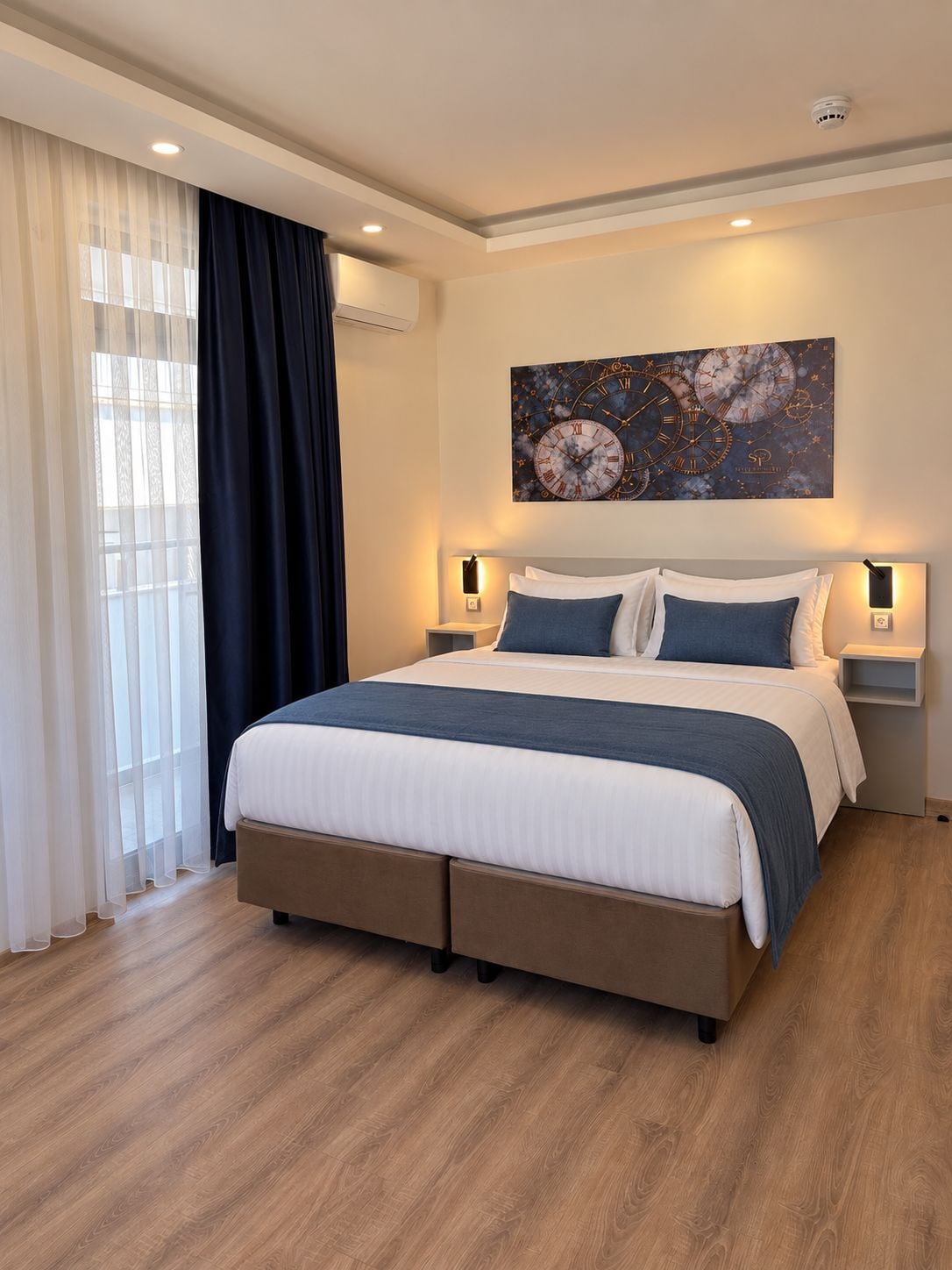 A modern bedroom with a large bed, two bedside tables, a wall clock, and a window with curtains.