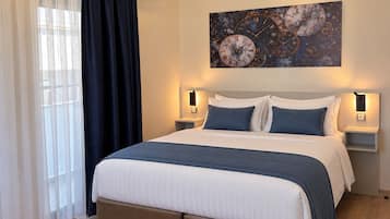 A modern bedroom with a large bed, two bedside tables, a wall clock, and a window with curtains.