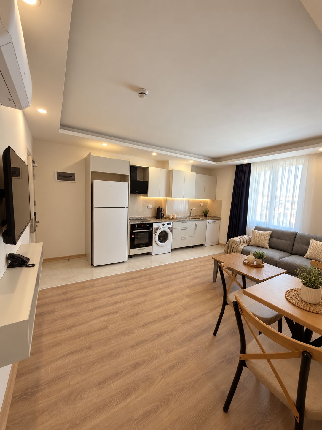 Een moderne keuken met een koelkast, oven en wasmachine. Er is een eethoek met een tafel en stoelen.