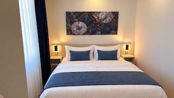 Une chambre d’hôtel avec un grand lit, deux tables de chevet, un luminaire fixé au plafond et une œuvre d’art accrochée au mur.