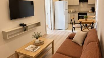 A modern living room with a sofa, a coffee table, a flat-screen TV, and a kitchen in the background.