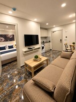 A modern living room with a sofa, a TV, a coffee table, and a kitchen area with a washing machine.