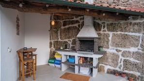 Un área de cocina al aire libre construida con piedra, con una parrilla empotrada, una mesa de madera y un banco.