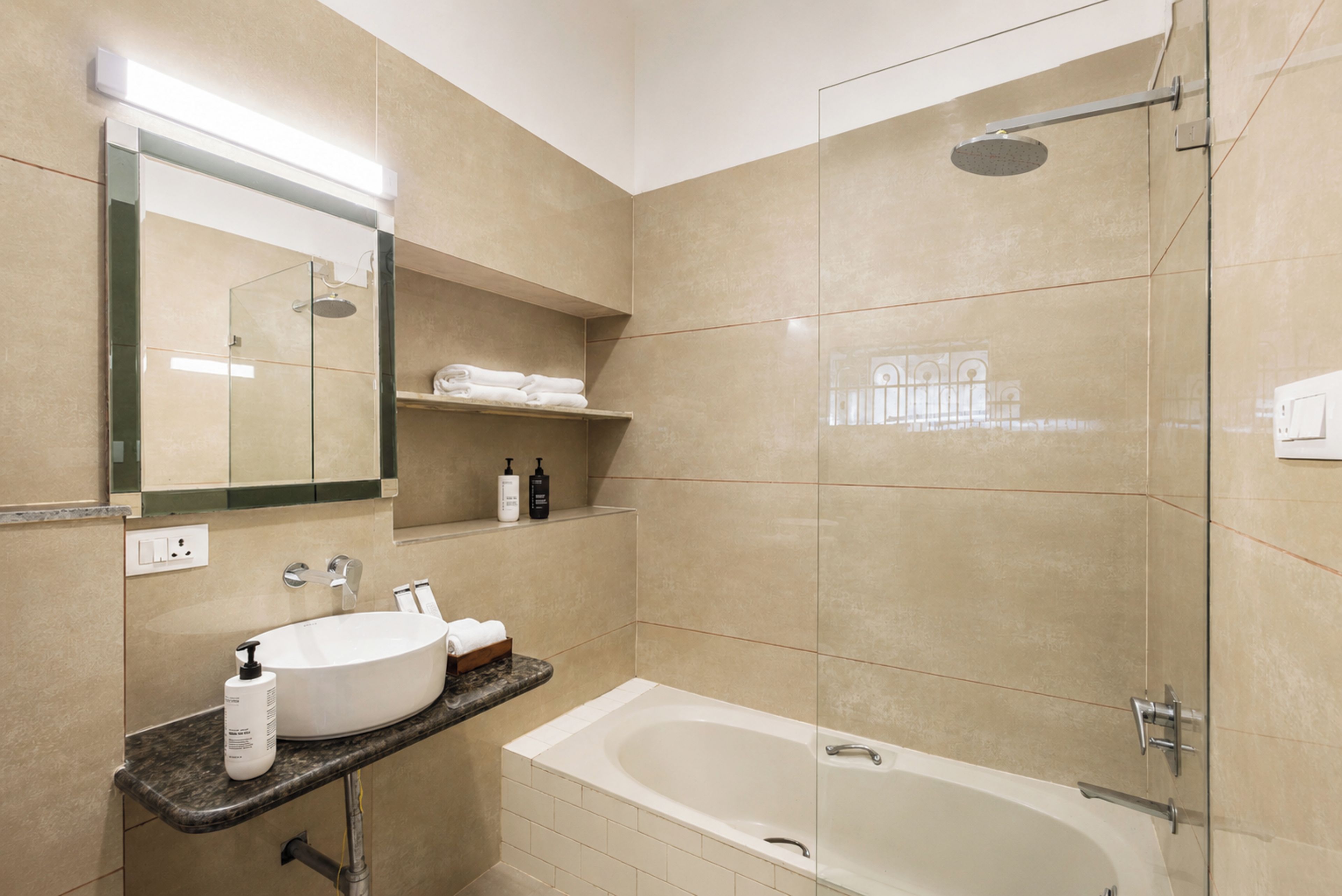 A bathroom with a bathtub, a shower, a sink with a mirror, and shelves with towels.
