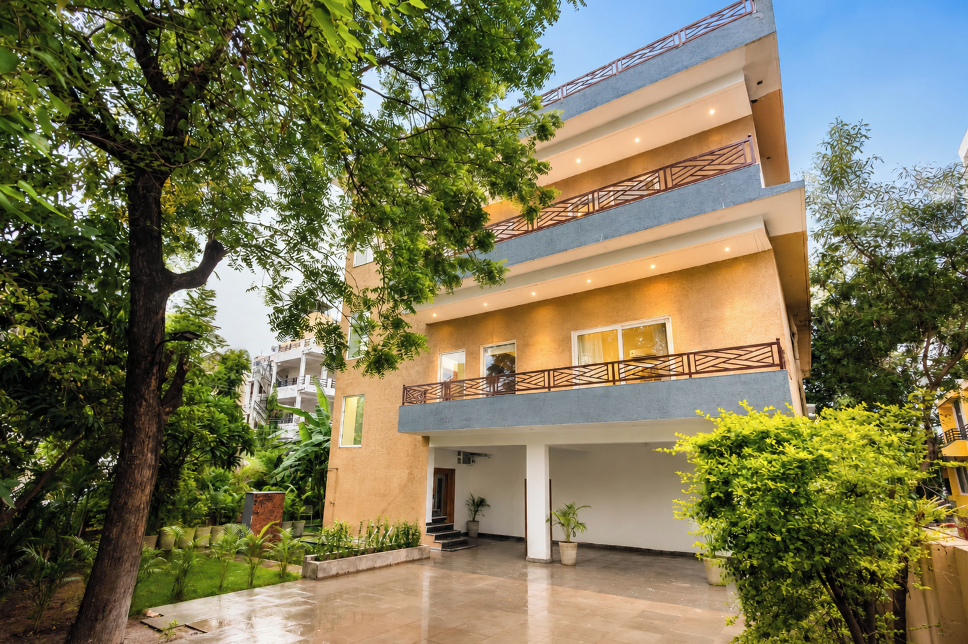 A multi-story building with a balcony, surrounded by greenery and trees.